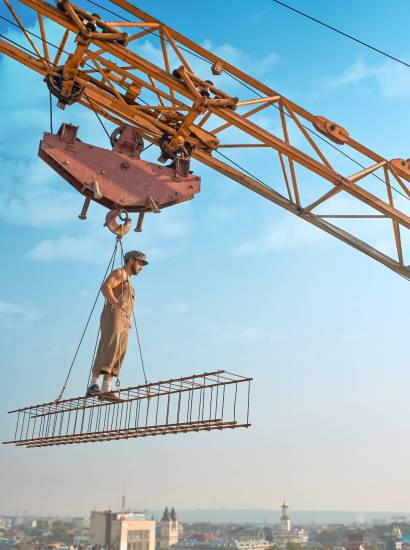 View from distance of athletic builder in work wear standing on construction on high. Building crane holding construction with man over city. Extreme building of house in big city. Man looking down.